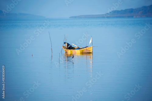 Fototapeta Naklejka Na Ścianę i Meble -  fishing boat and fisherman standing in lake water in foggy weather, golyaka uluabat lake