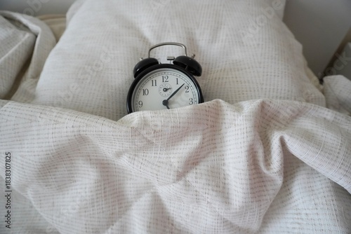 Black analog alarm clock under a blanket close-up, soft light, fabric texture. Topic: morning, daily routine. The black vintage alarm clock is asleep. Horizontal image.