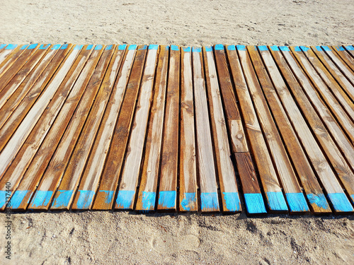 Wooden slats of a roll-up boardwalk on the sandy beach. Close-up of a wooden walkway providing access to the beach. Structure to facilitate beach access.