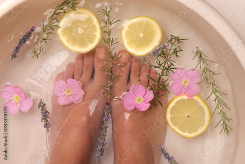 Photos Studio shot of female feet soaking in water bowl with lemon slices, rosemary, lavender and pink flowers for natural spa treatment