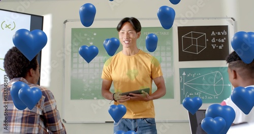 Presenting pupil wearing yellow tee, jeans holding tablet in class with periodic table, blue hearts