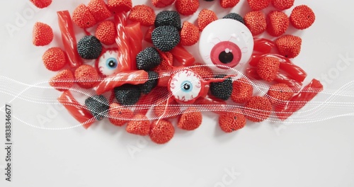 Showing top-down candy on white table, raspberry or blackberry, licorice, 3 eyeballs, dotted-wave