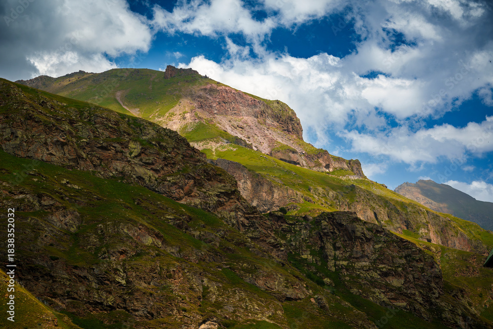 Obraz premium Green mountain slope with rocky cliffs and snowy peaks in the distance