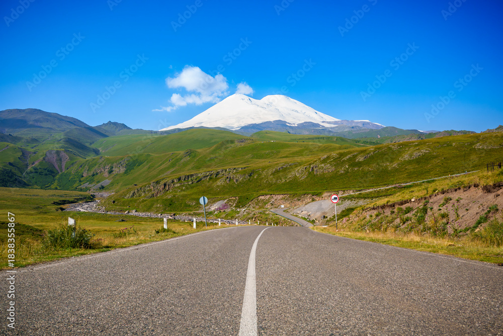 Fototapeta premium Road leading to Mount Elbrus with snow-covered peak and blue sky