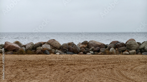 A structure made of large piled rocks protecting the beach on the shore of a large lake. Gray sky and gray water in inclement weather. Background.