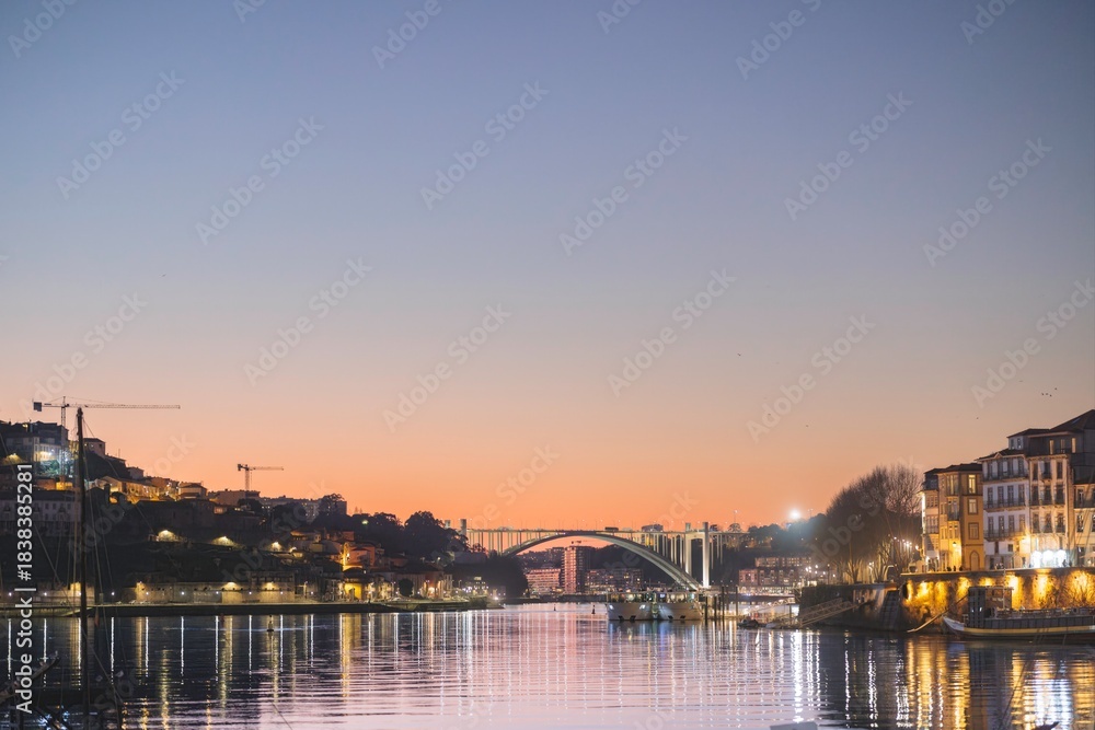Fototapeta premium The evening light paints the city of Porto, Portugal as twilight settles. Gentle reflections ripple across the Douro River at dusk