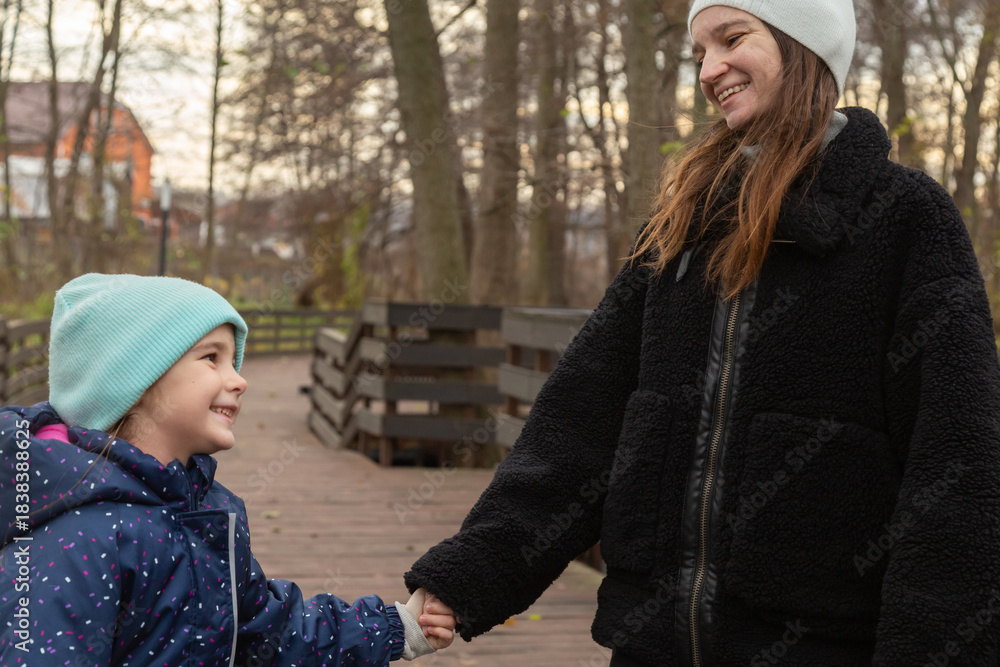 Fototapeta premium Mother and daughter holding hands as they walk together in park. Mother and daughter walking hand in hand in the park in autumn. Happy family outdoors.