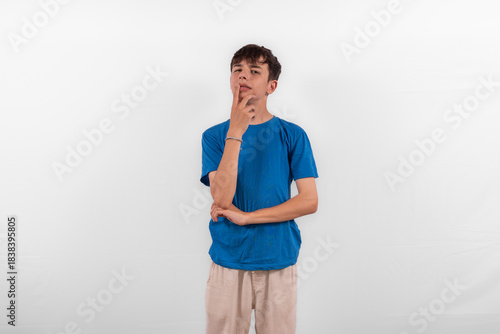 young casual dressed white male model teenager with hand on chin expression is pensive, pondering, considering or thinking about something. plain background studio setting