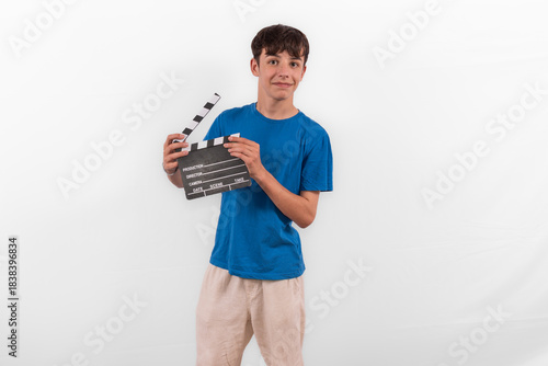 young happy casual dressed Generation Z influencer white male model teenage boy prepares to create and direct fun social media film reel with blank clapperboard slate. plain background studio setting
