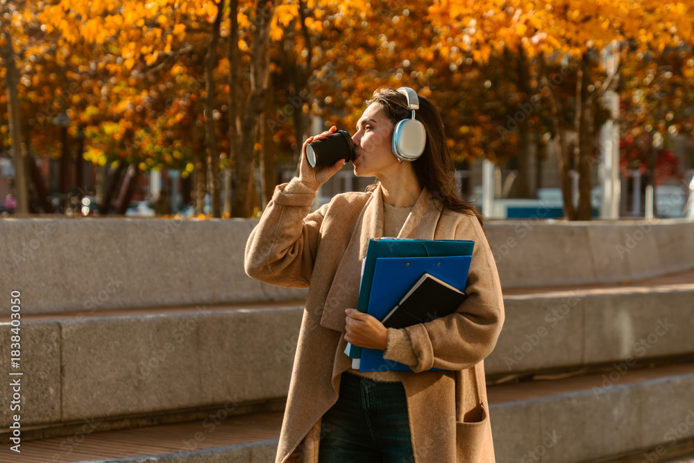 Naklejka premium Woman Walking with Headphones and Coffee in Autumn City