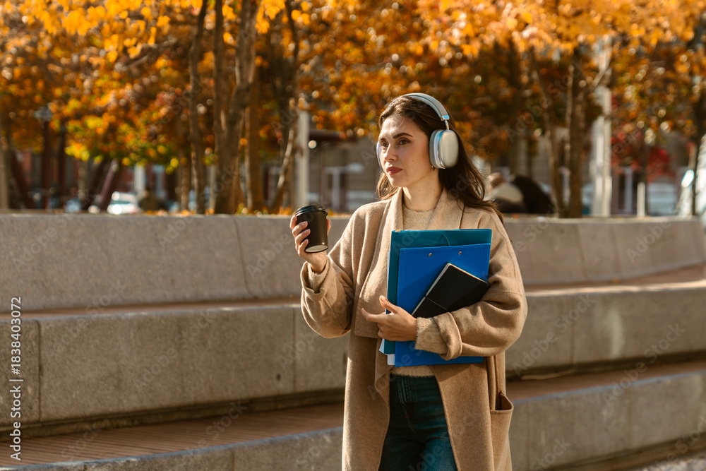 Naklejka premium Woman Walking with Headphones and Coffee in Autumn City