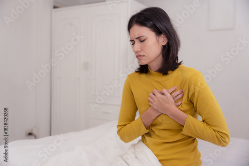 Young woman in bed clutching her chest in pain, showing signs of heart disease, chest pain, or anxiety attack, concept of cardiovascular health, emotional distress, and emergency symptom.