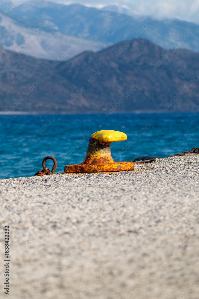 Obraz premium Rusty yellow mooring bollard on a pier with sea and mountain background