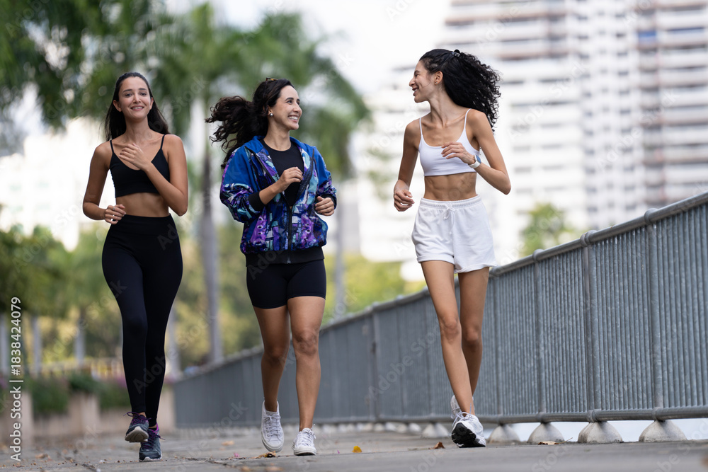 Obraz premium Three fit young women in sportswear jogging together on an urban park path, enjoying a healthy morning workout and happy friendship moments in nature.
