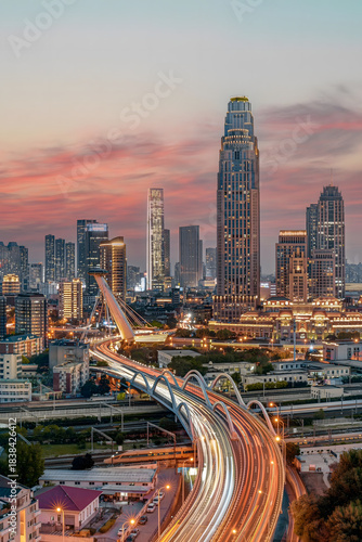 Fotografía Tianjin City Skyline at Dusk with Illuminated Skyscrapers and Light Trail Highwa