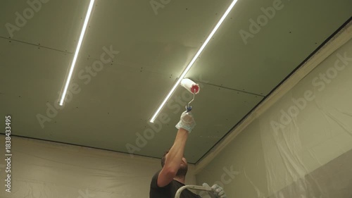 A man primes a drywall ceiling with a roller