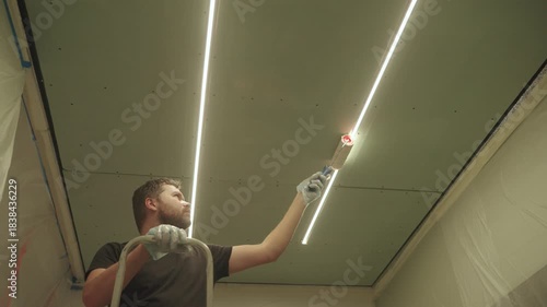 A man primes a drywall ceiling with a roller