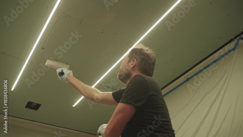 A man primes a drywall ceiling with a roller