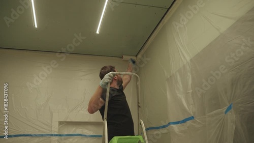A man primes a drywall ceiling with a roller