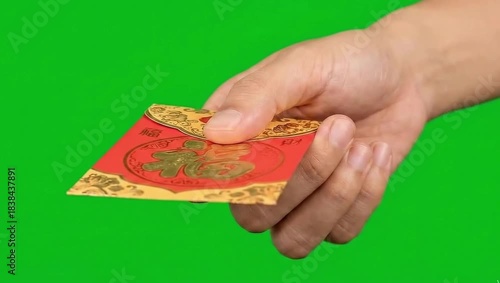 Hand holding a red envelope with golden Chinese characters, symbolizing good fortune and wealth, on a green background