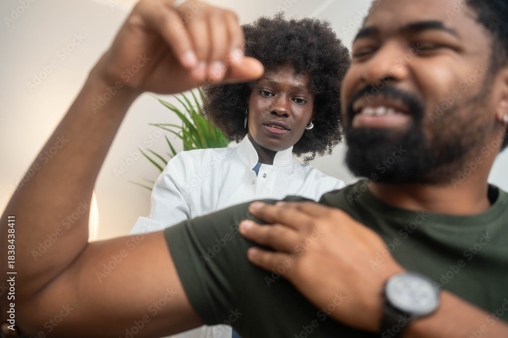 Obraz premium Black female physiotherapist assisting male patient with shoulder exercises in clinic
