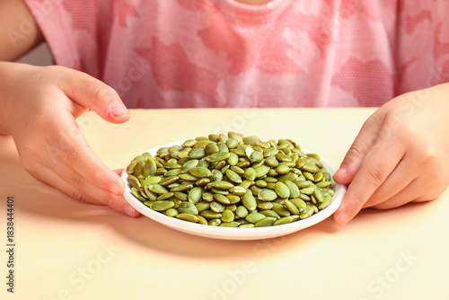 Canvas-taulu Child Holding Bowl of Shelled Green Pumpkin Seeds Studio Shot