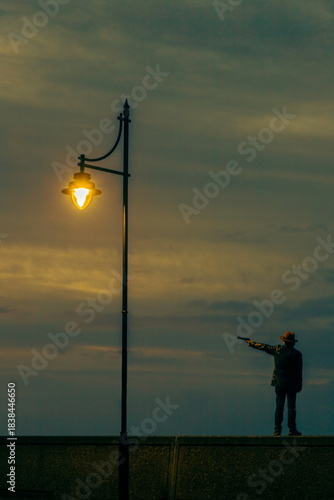 Man with a hat holding gun under lamppost at dawn