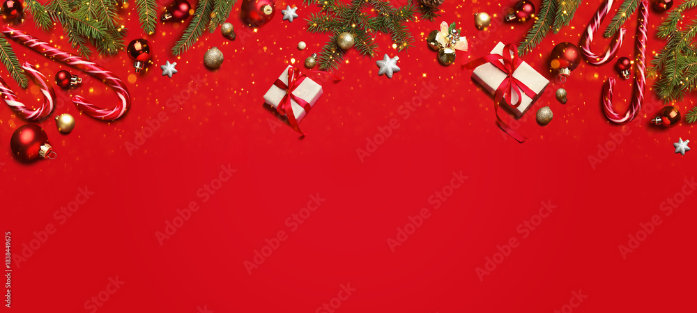 Fototapeta premium Christmas balls, gift boxes, fir branches and candy canes on red background, top view. Greeting card or poster with space for text