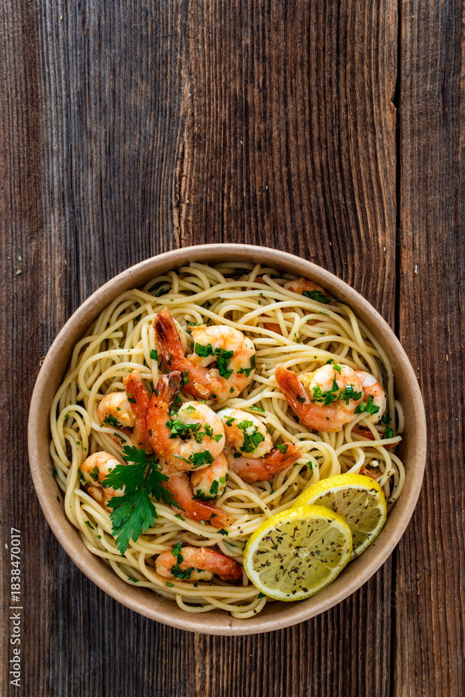 Fototapeta premium Takeaway food - fried shrimps with noodles and lemon in lunch box to go on wooden table