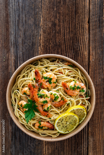 Takeaway food - fried shrimps with noodles and lemon in lunch box to go on wooden table
