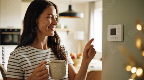 Woman adjusting smart thermostat holding hot drink indoors at home controlling energy efficiency and comfort daily life scene
