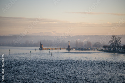 Lake Constance and Constance Harbor with snow-covered Säntis mountain in the background during a pastel-colored winter evening. Konstanz, Baden-Württemberg, Germany.
