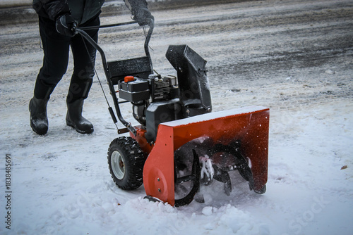 Front and side view of a person using a gas snow blower to clear snow off of a driveway. lifestyles and weather with copy space. Winter weather design element. Meteorology or news.