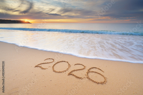 2026 year text symbol on the sea sand beach shore during sunset.