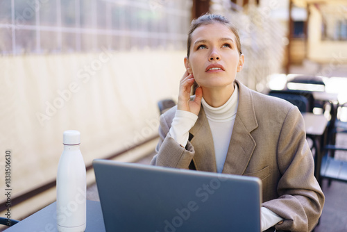A Thoughtful Woman Engaged in Productive Work Outdoors with a Laptop and Water Bottle