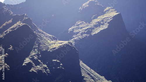 Majestic mountain peaks rise dramatically against a soft dawn light, revealing rugged textures and a touch of green. The tranquility of the landscape invites exploration and introspection.