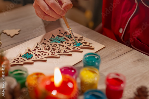 Children's hands paint wooden toy Christmas tree with candles on table