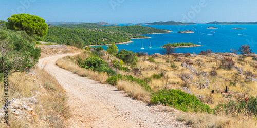 Croatian coastal landscape with small islands in the sea, green forest and blue water, view from a gravel bike path on a hill on a sunny day.