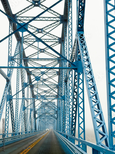 Going over a two-lane blue truss bridge on a foggy day.