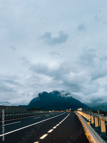 Winding highway stretching through mountain valley under cloudy sky during tranquil evening, evoking serene and peaceful atmosphere perfect for reflection and exploration. Scenic mountain backdrop