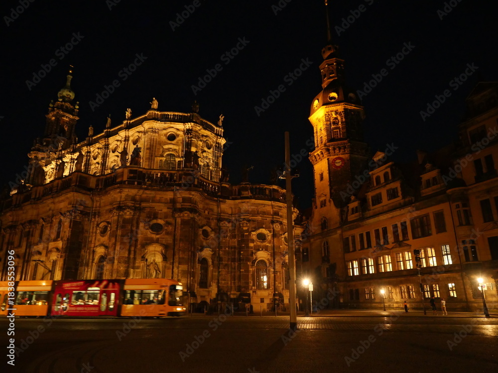 Fototapeta premium Illuminated tram in front of historic architecture in Dresden at night. Catholic Court Church. Copyspace