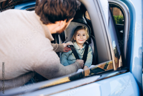 Obraz na płótnie Father buckling child, cute little girl into car seat for safety