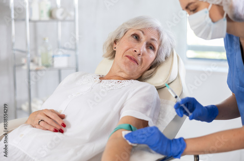 Adult woman with grey hair is receiving injecting hypodermic against covid or flu.