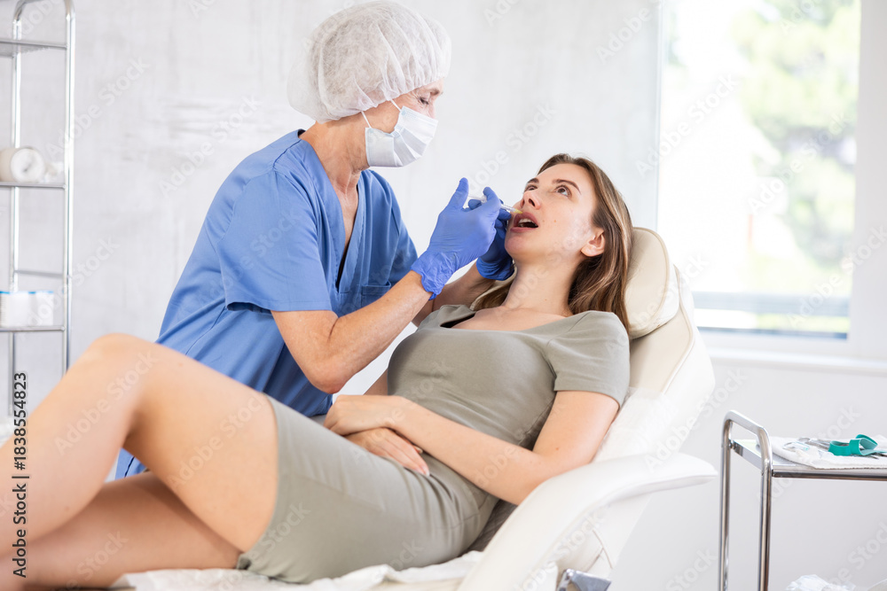 Obraz premium Young brunette woman having facial injection at bright treatment room with big window at background at aestetic center
