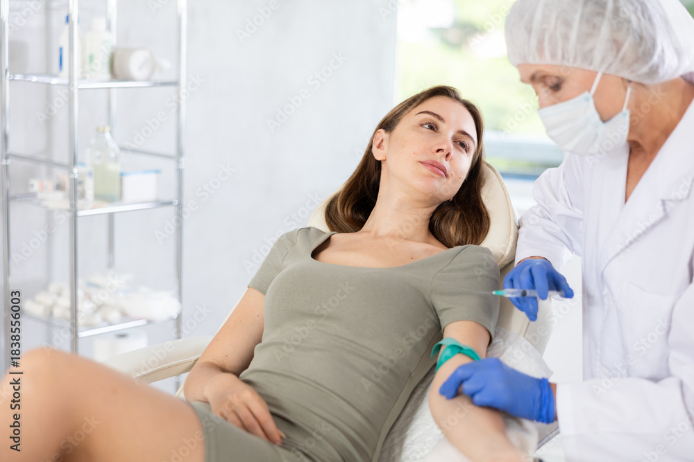 Fototapeta premium Young long-haired girl lying at white examination couch before intravenously injection at treatment room