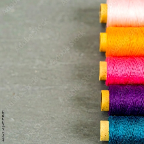 Colorful sewing thread spools in a row against a gray surface