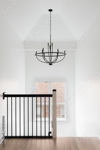 A hallway and staircase with a wrought iron railing, hardwood floor, and chandelier hanging from the tall ceiling.