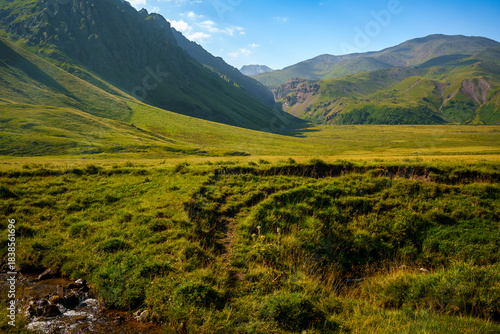 Green mountain valley with rocky slopes under clear blue sky