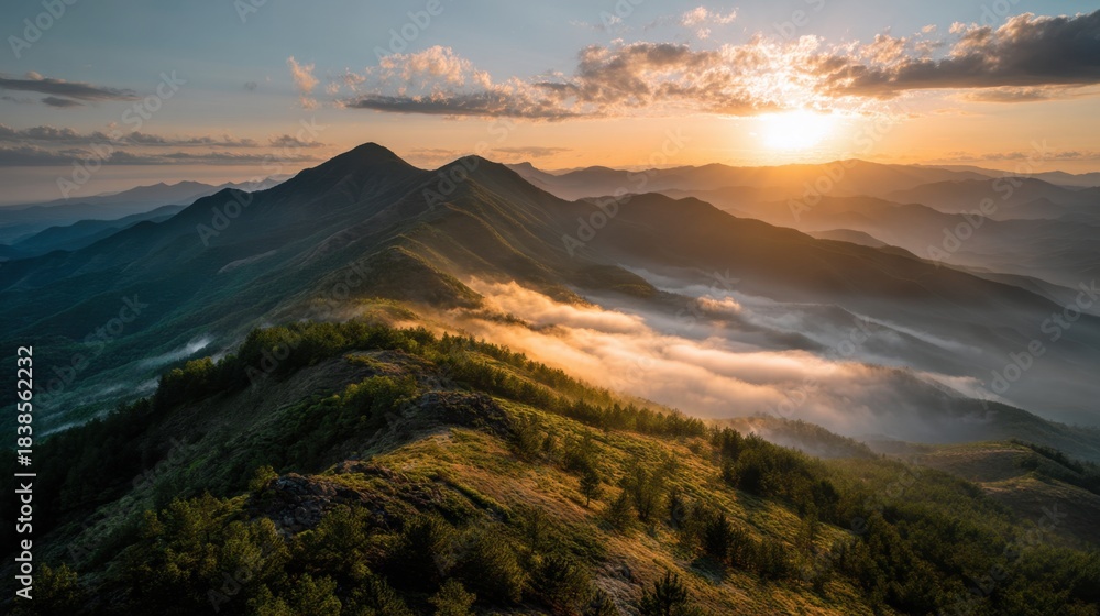 Obraz premium The sun rises over a mountain range casting light on mist that fills the valleys. Hills are visible in the distance with trees scattered across the landscape.