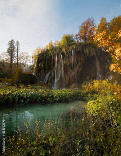 Canvas Print tranquil morning scene in plitvice national park in croatia, showing a waterfall surrounded by trees with fall colors of orange, red, and yellow, and a small turquoise lake with reflections
